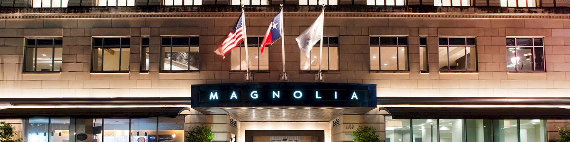 The image shows the entrance of a building with the sign “Magnolia” and three flags above it, likely a hotel or similar establishment.