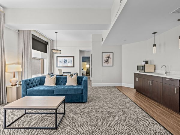 The image shows a modern living area with a blue couch, coffee table, kitchenette, and framed art on the walls, creating a cozy atmosphere.