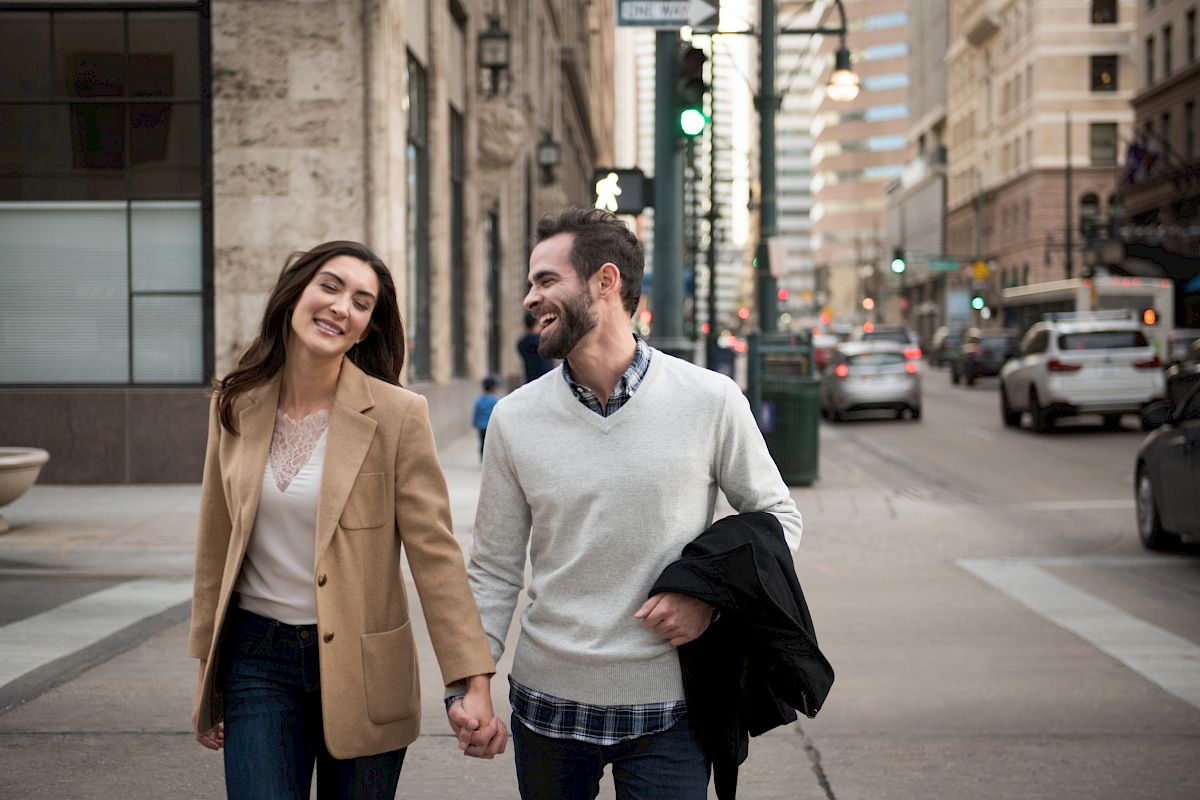 A couple is walking hand in hand on a city street, smiling and enjoying each other's company.