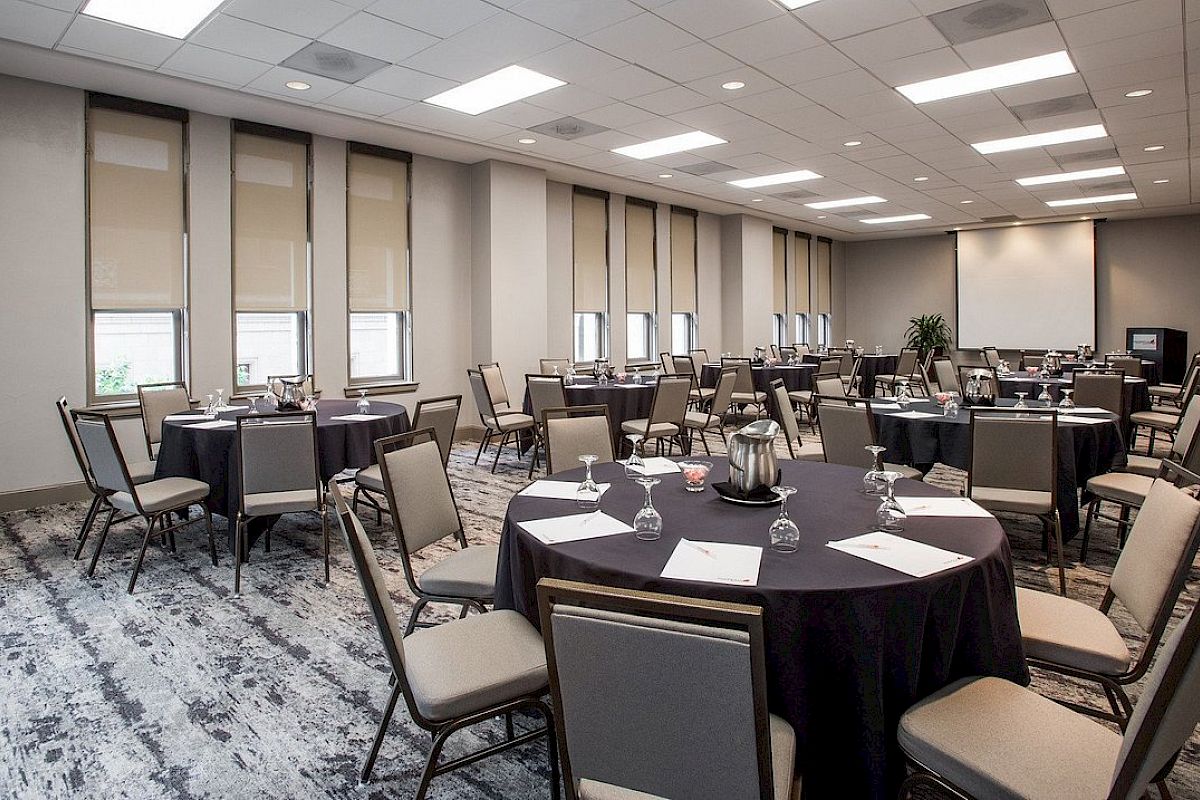 The image shows a conference room set with round tables, chairs, paper, and glasses, ready for an event or meeting.