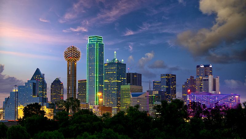 A city skyline at dusk with many skyscrapers and a prominent spherical building.