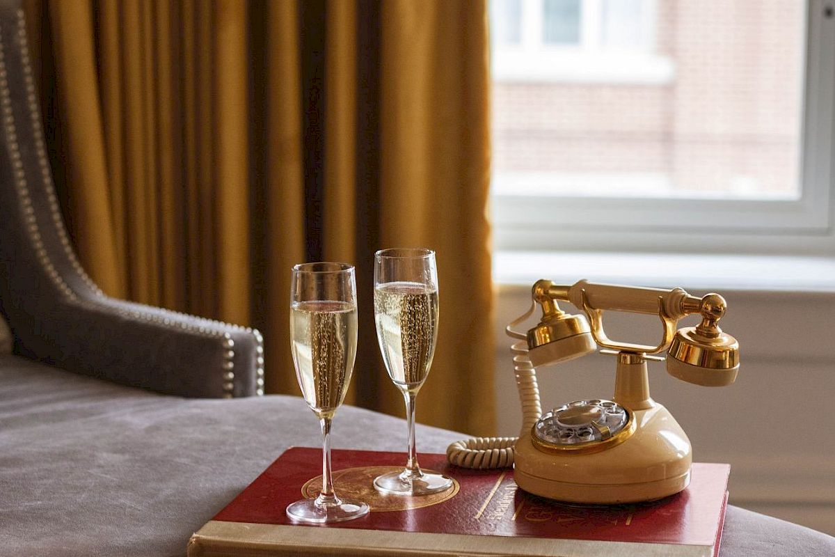 A luxurious setting with two filled champagne glasses and a vintage phone on a tray by a window with yellow curtains.