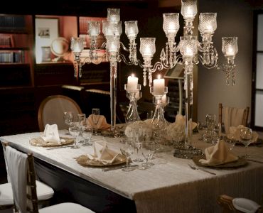 A formal dining table is set with elegant chandeliers, crystal glasses, and neatly folded napkins in a softly lit room.