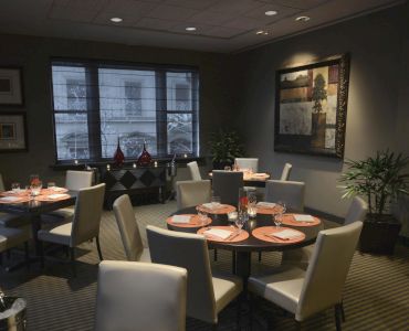 A modern dining room with round tables, white chairs, and elegant decor. Tables are set, and artwork adorns the walls.