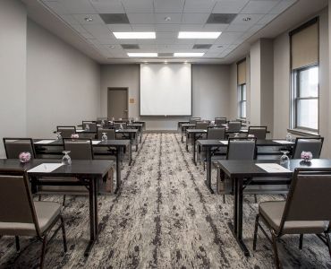 The image shows an empty conference room with rows of tables and chairs facing a projection screen, ready for a meeting or presentation.