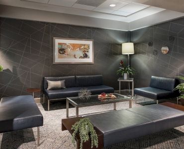 A modern waiting room with sleek black furniture, geometric wall designs, plants, and a framed artwork. A calm and inviting atmosphere.