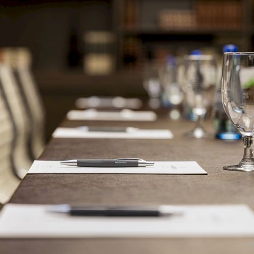 A conference table is set with notepads, pens, water bottles, and glasses, ready for a meeting or presentation.