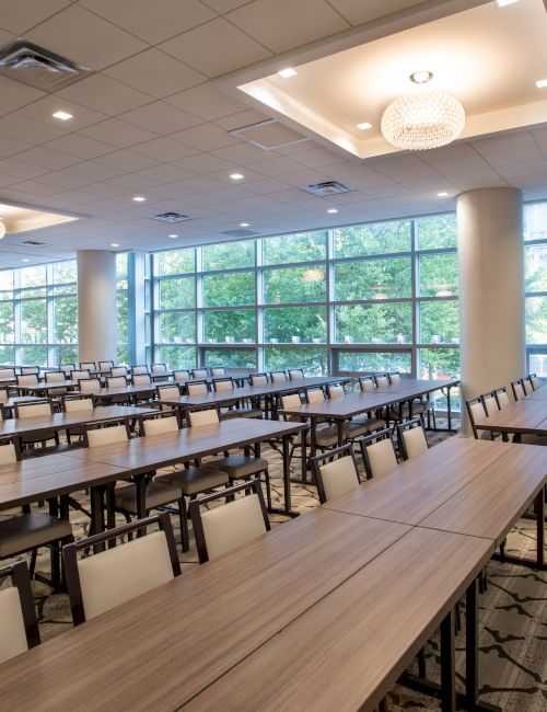 A modern conference room with long tables and chairs, large windows, and bright lighting, ready for an event or meeting.
