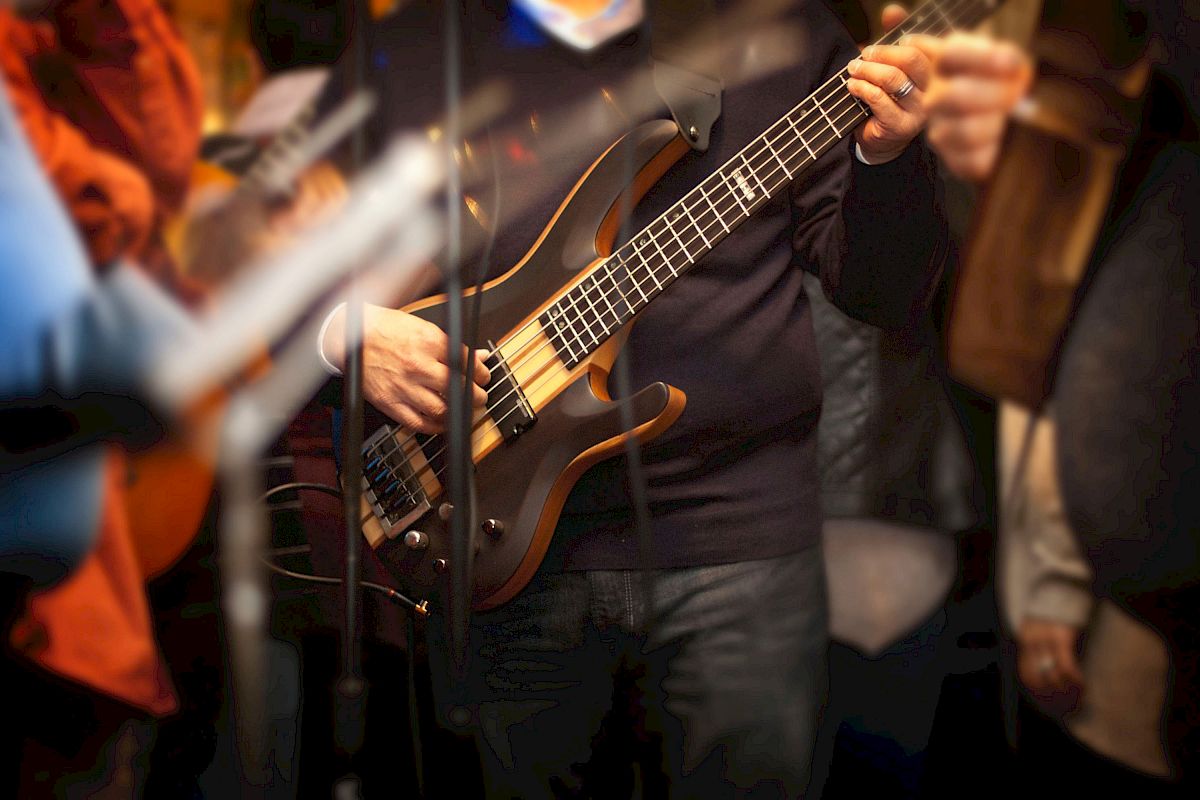 A person is playing an electric bass guitar during a performance. Other musicians and instruments are partially visible around them.