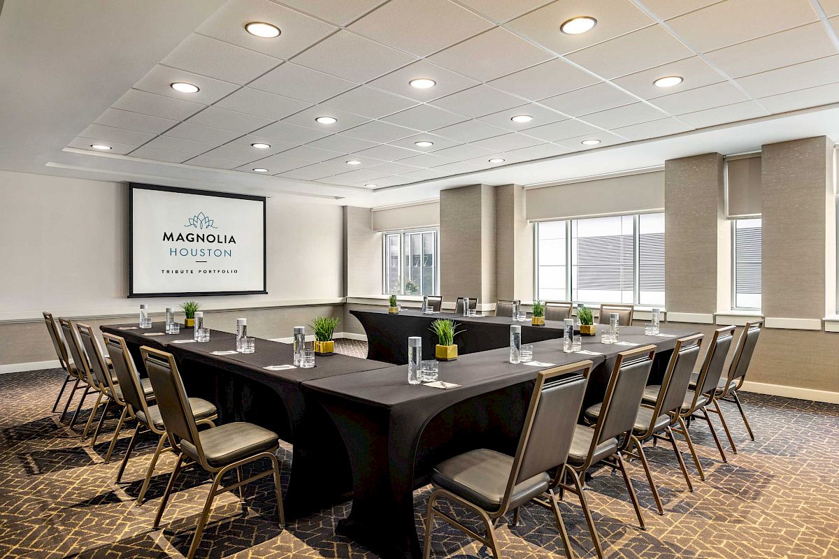 A conference room with a U-shaped table setup, chairs, water glasses, and a screen displaying