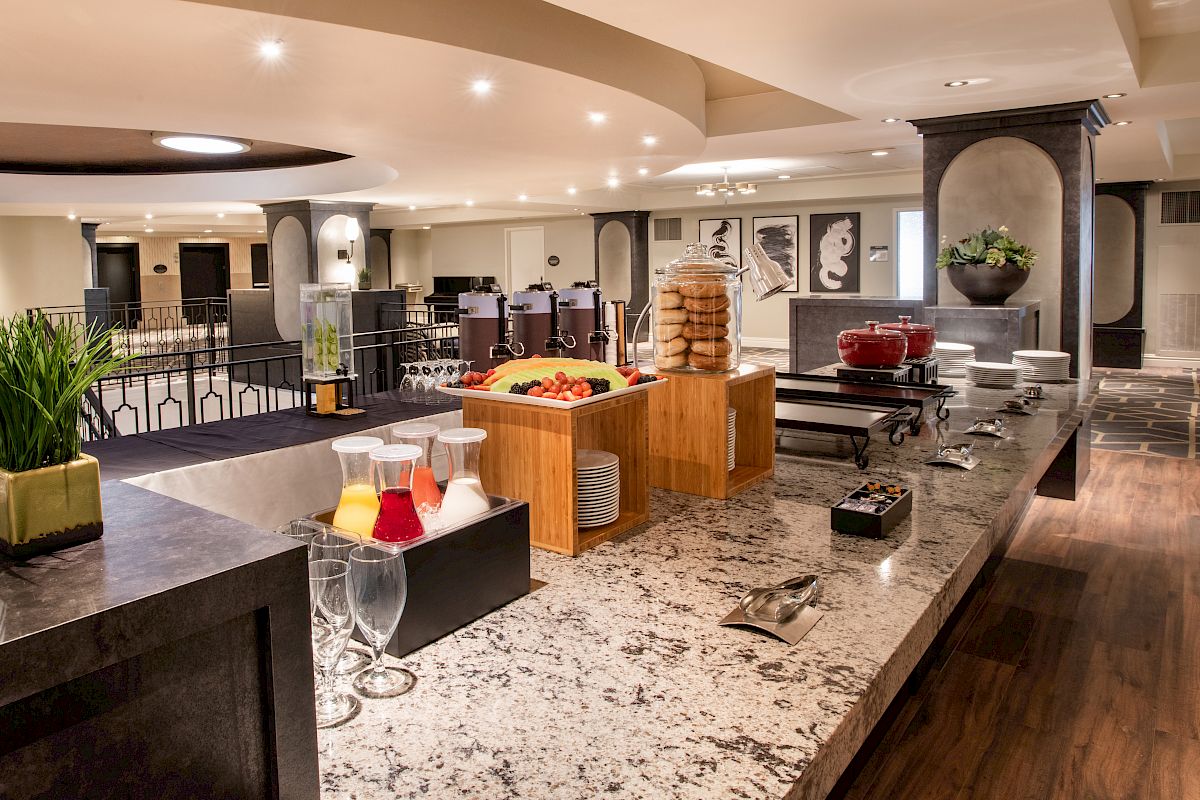 The image shows a buffet setup with drinks, fruits, and cookies on a granite counter in a spacious and well-lit dining area.