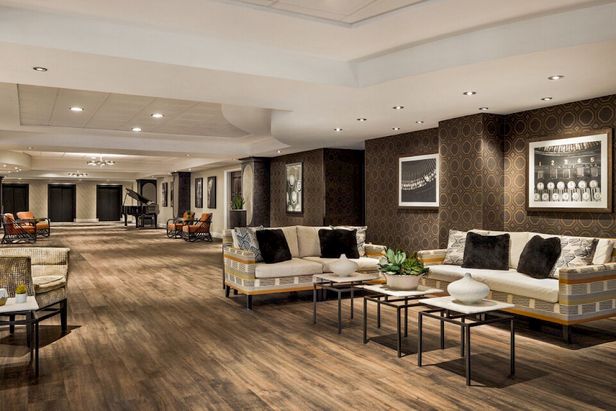 A spacious hotel lobby with modern seating, wooden flooring, and framed artwork on the walls. It has a warm, welcoming atmosphere.