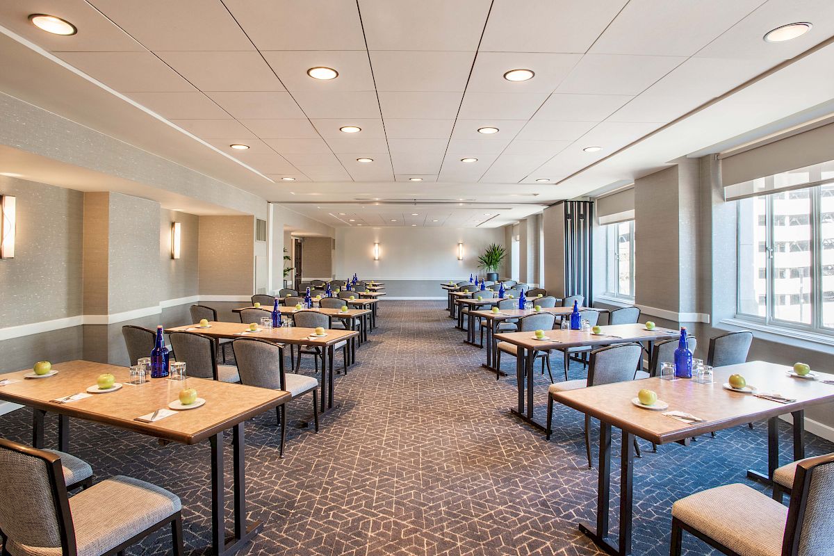 A modern conference room with multiple tables and chairs, neatly set with water bottles and notepads, ready for a meeting or event.