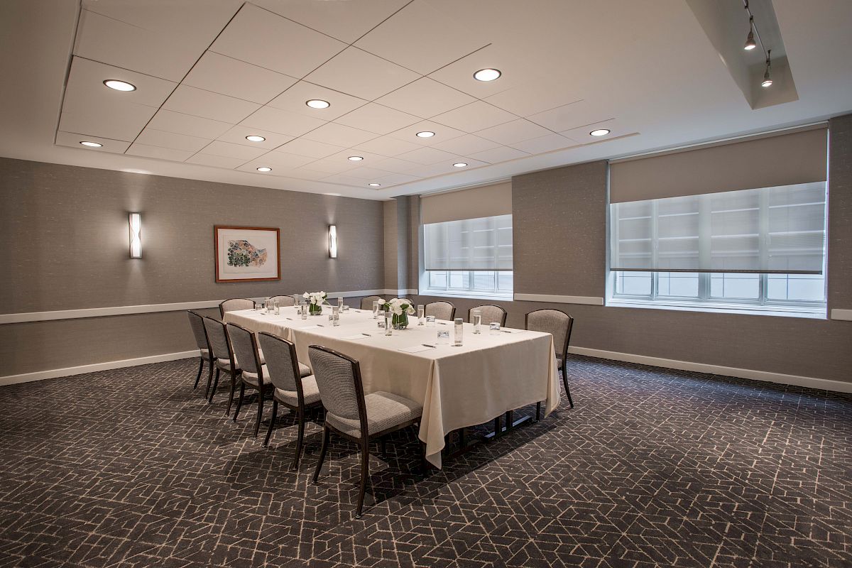 A conference room with a U-shaped table setup, surrounded by chairs, with lighting and blinds drawn.