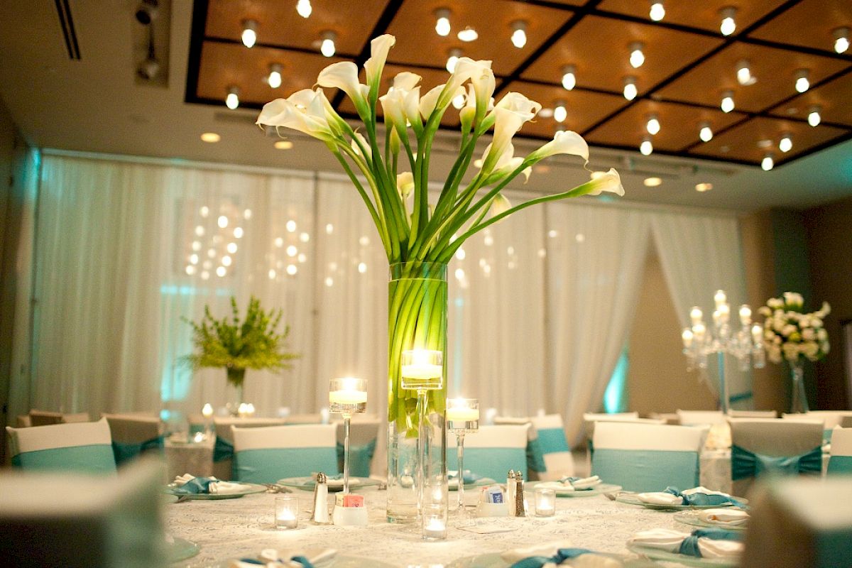 Elegant table setting with white flowers, candles, and teal accents in a softly lit room.