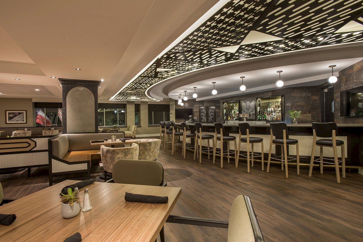 The image shows a stylish restaurant interior with a bar, modern seating, and contemporary design elements, featuring warm lighting and decor.