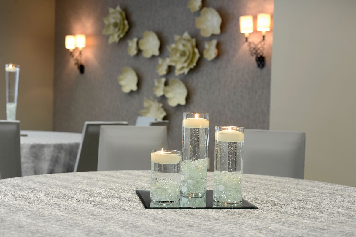 A table with three glass candle holders, floral wall decor, and soft wall lighting in a modern room setting.