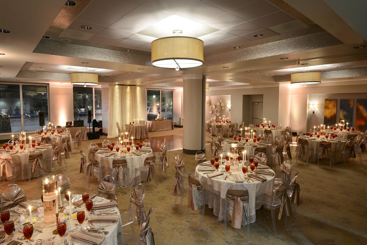 An elegantly decorated banquet hall with round tables, white tablecloths, red drinks, and ambient lighting, ready for an event.
