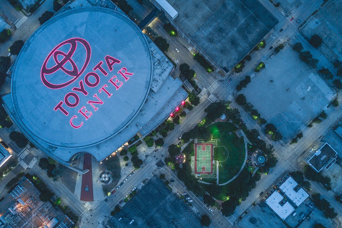 Aerial view of the Toyota Center and surrounding streets at night, with a lit basketball court nearby, in an urban setting.