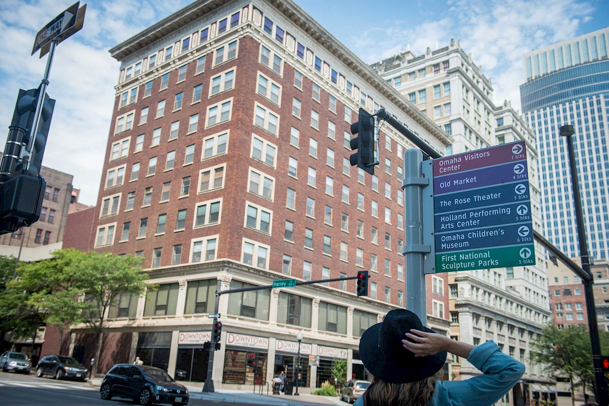A person looks at a street sign displaying local attractions in an urban area with tall buildings and clear skies in the background.