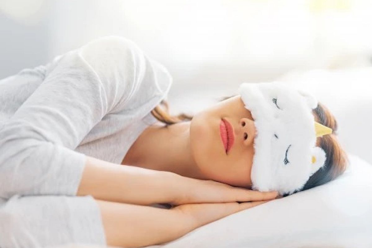 A person is sleeping in bed, wearing a whimsical eye mask shaped like a unicorn.