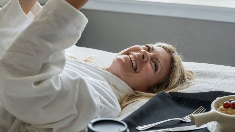 A person is lying on a bed reading a book, with breakfast and a coffee on a tray beside them.
