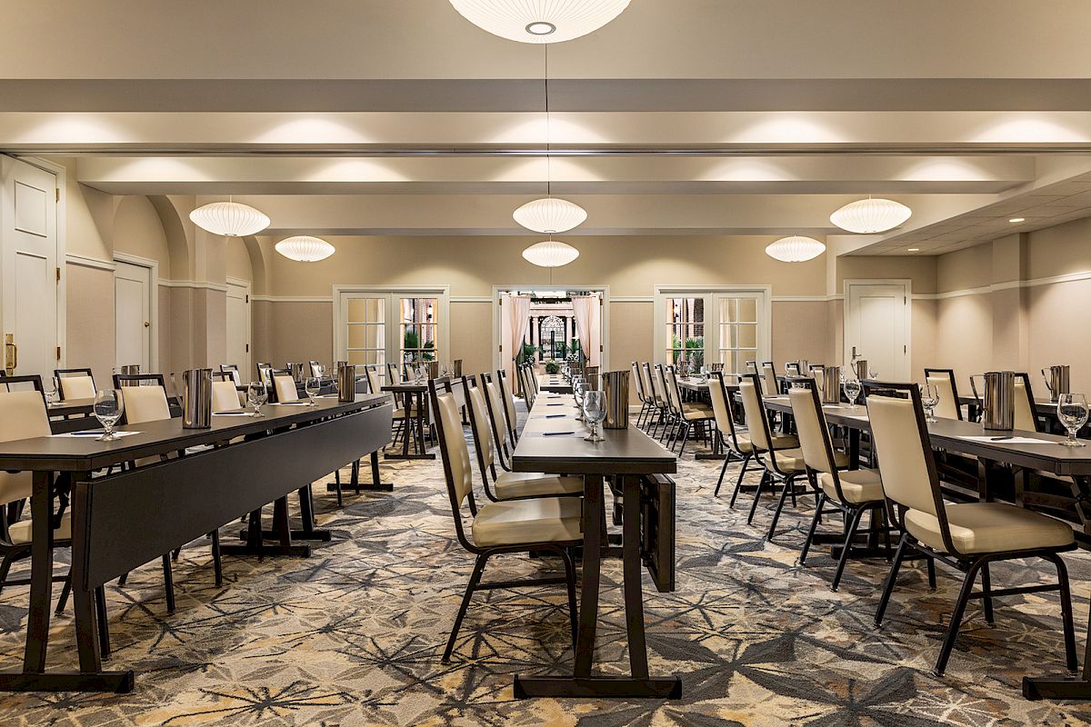 The image shows an empty conference room with rows of tables and chairs, neutral decor, and overhead lighting, ready for a meeting or event.