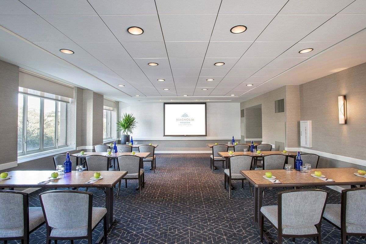 A modern conference room with tables, chairs, water bottles, and notepads arranged, facing a screen displaying a logo or presentation.