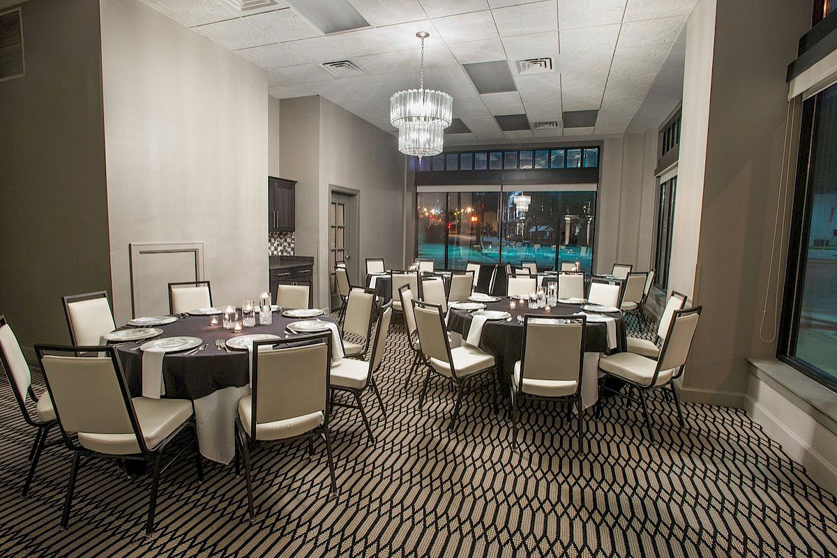 The image shows a banquet-style dining room with round tables, set with plates and glasses, and elegant white chairs around each table.