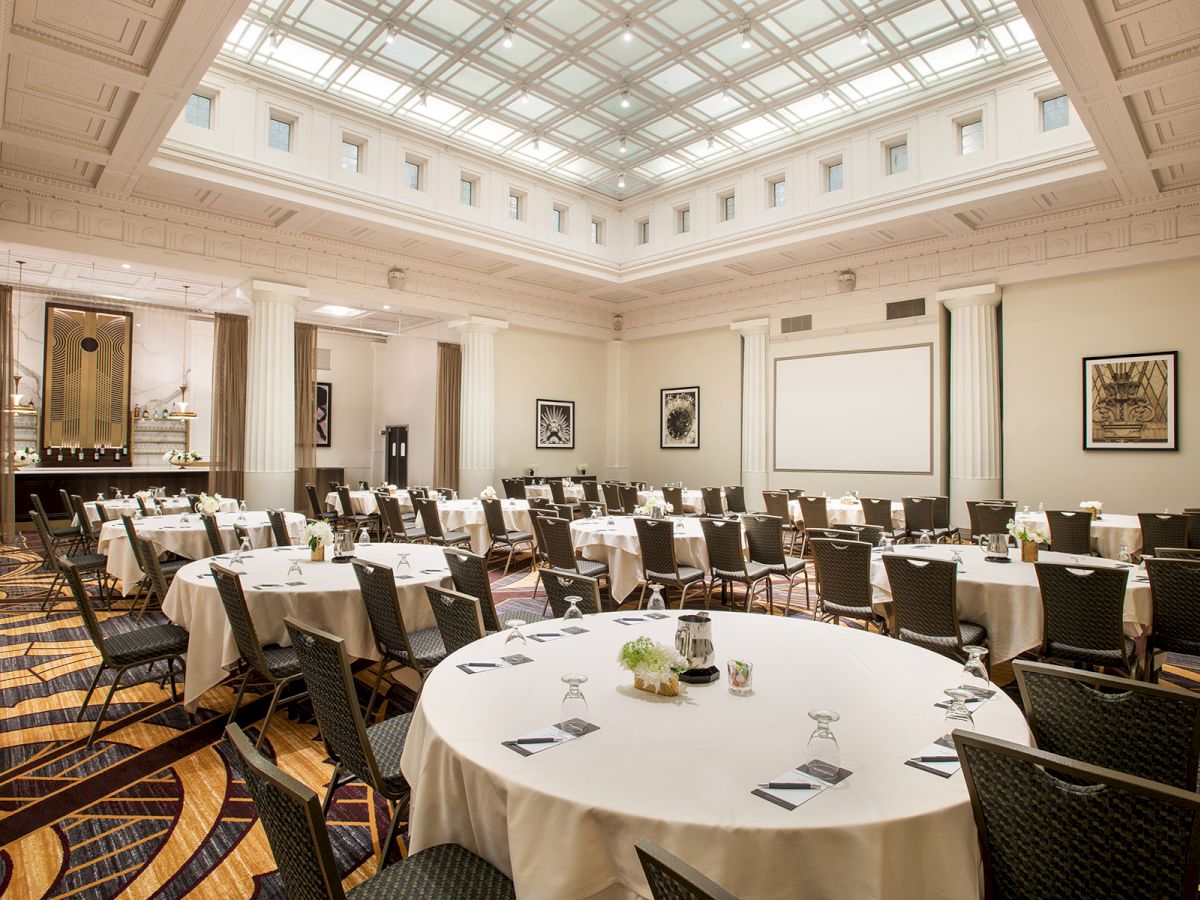 The image shows a spacious, elegantly decorated conference room with round tables and chairs arranged for an event or meeting.