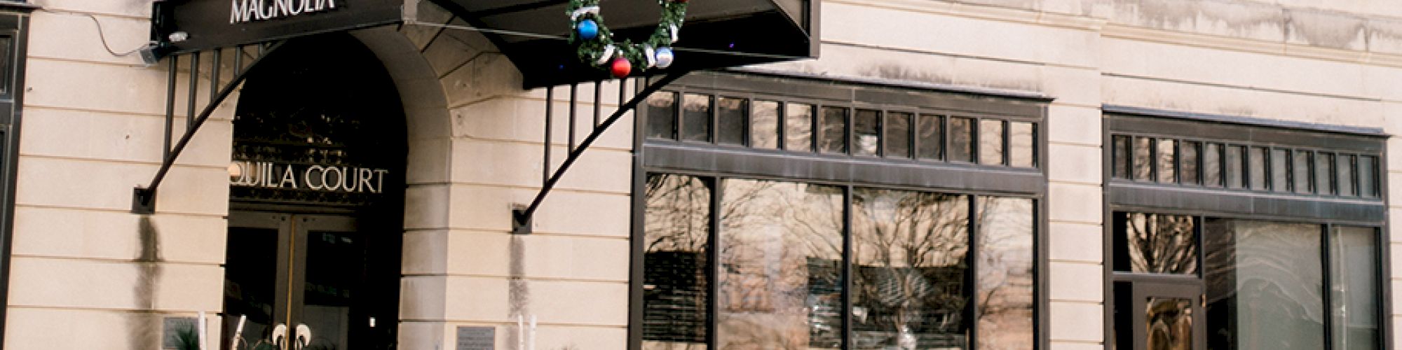 The image shows the entrance of Magnolia hotel with a wreath above the entrance and decorative plants on both sides.