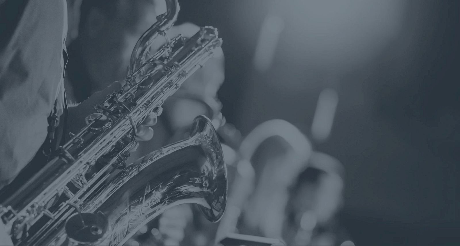 A monochrome image of a saxophone player in a band, with blurred figures in the background, under stage lighting.