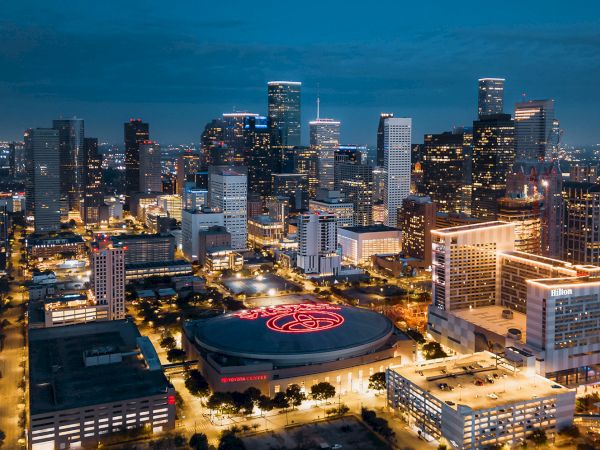 The image shows a nighttime view of a city skyline with many lit skyscrapers and a prominent arena in the foreground.