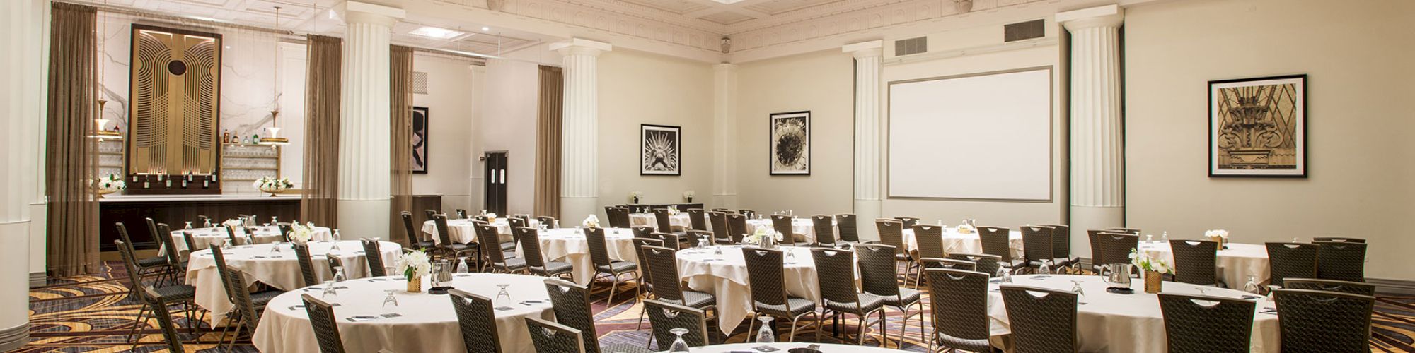 A conference room with round tables, chairs, a white screen, and decorative lighting.