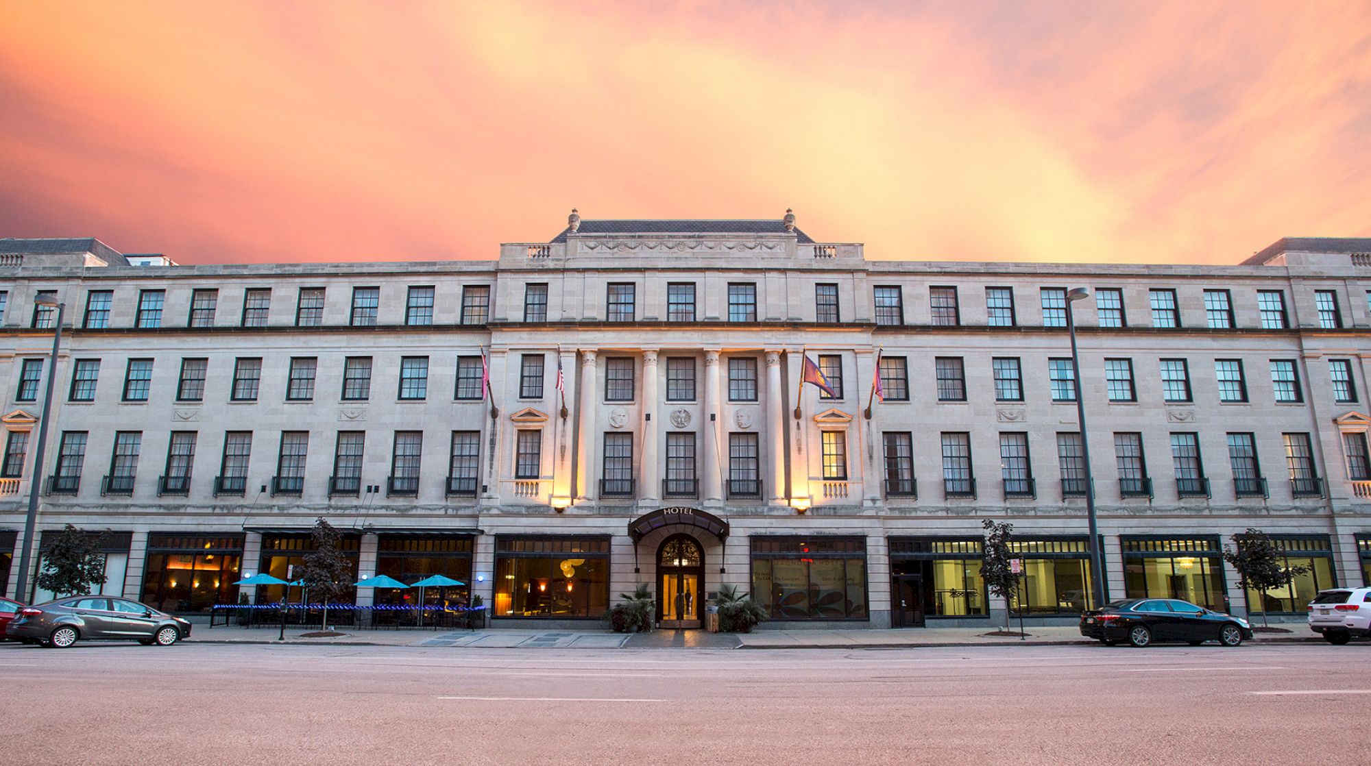 The image shows a large building with a symmetrical facade, featuring flags and a sunset sky in the background.