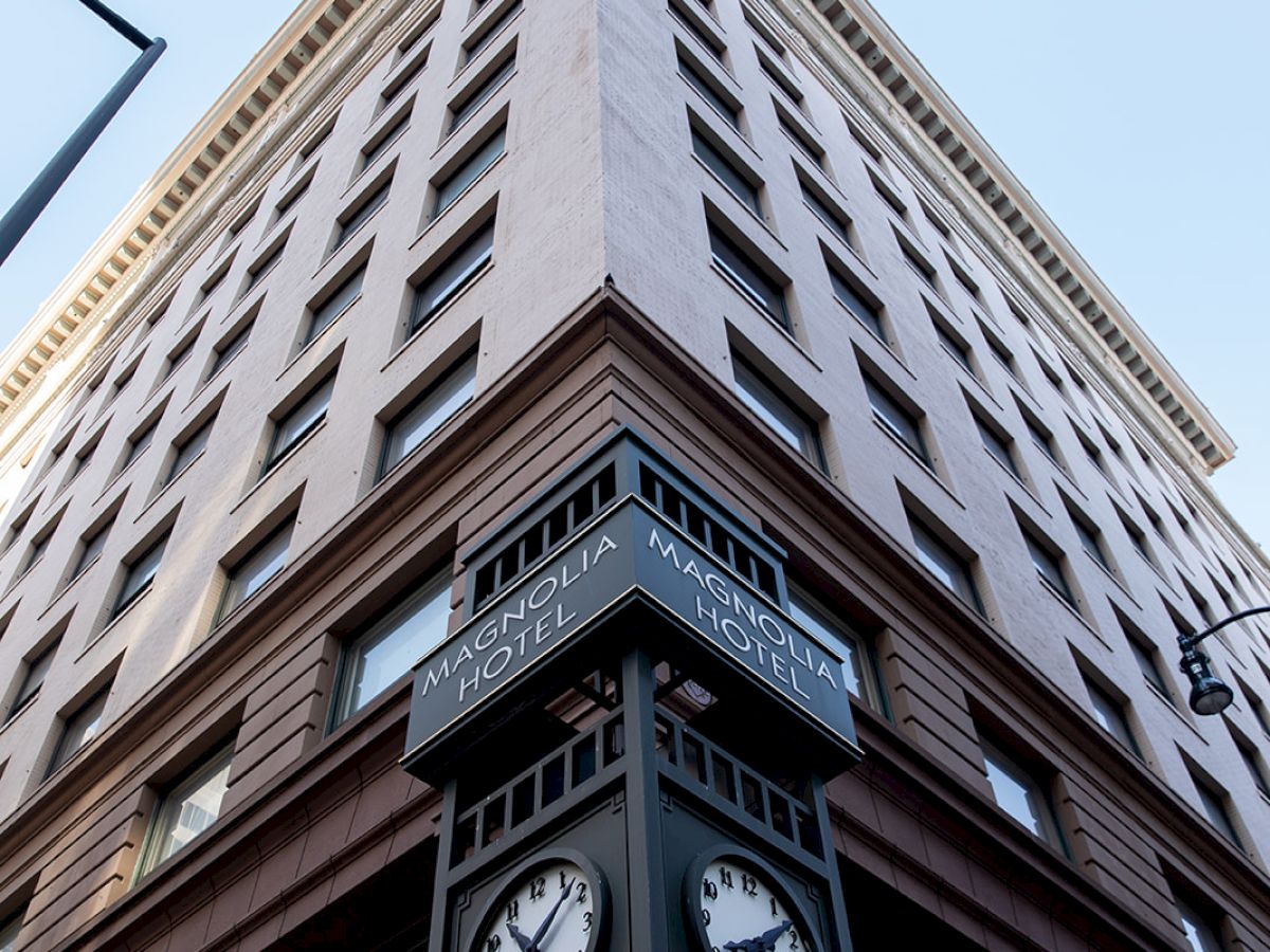 The image shows a tall corner building with a vintage clock on the corner. The clock is attached to a sign labeled 