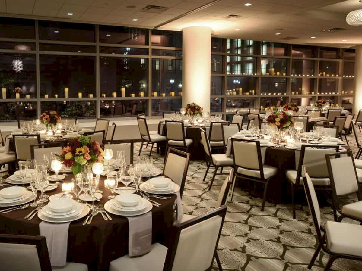 The image shows an elegant banquet hall with round tables set for a formal event, featuring floral centerpieces and candles.