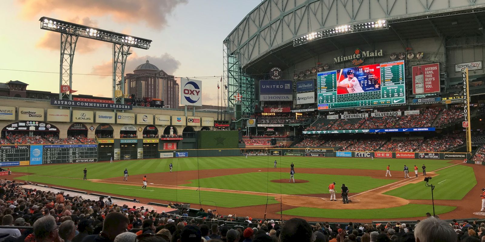 A baseball game in a domed stadium at sunset with a crowd, field, and large screen visible, creating an engaging sports atmosphere.