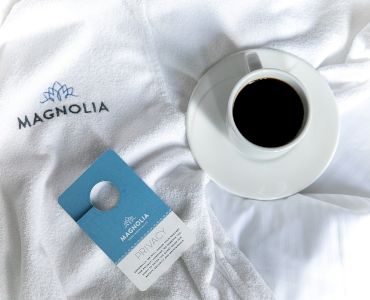 A white cup of black coffee sits on a Magnolia-branded towel beside a blue 