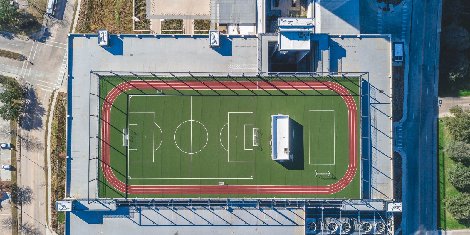 The image shows an aerial view of a rooftop sports facility with a soccer field and running track.