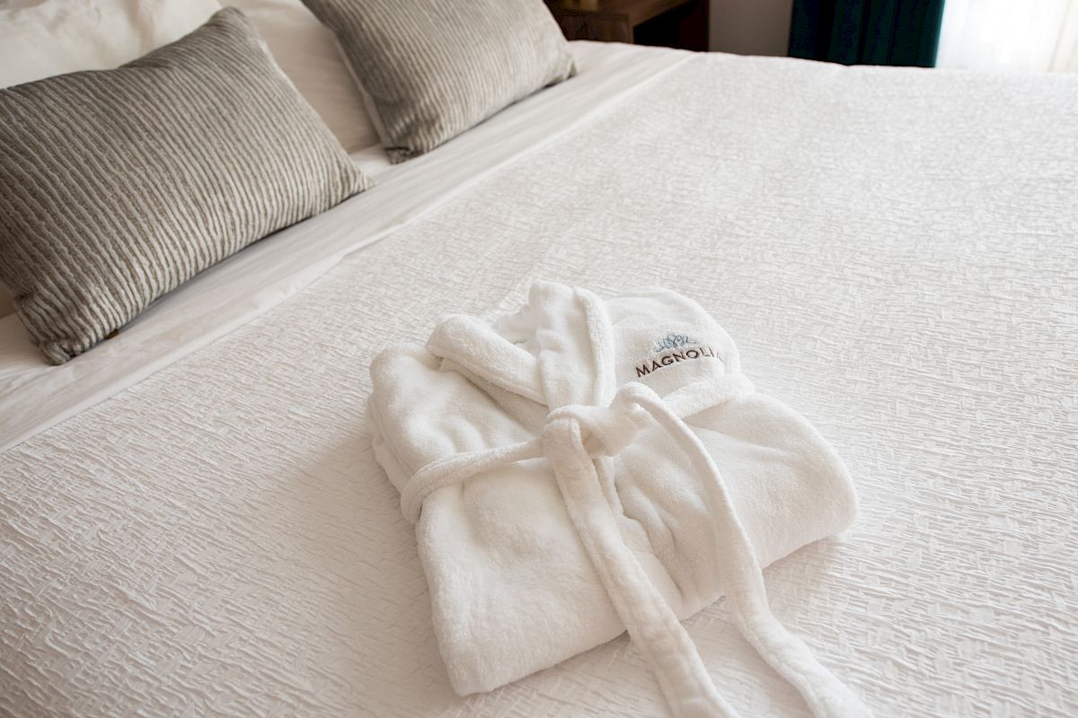 A white bathrobe is neatly folded on a made bed with gray pillows in the background.