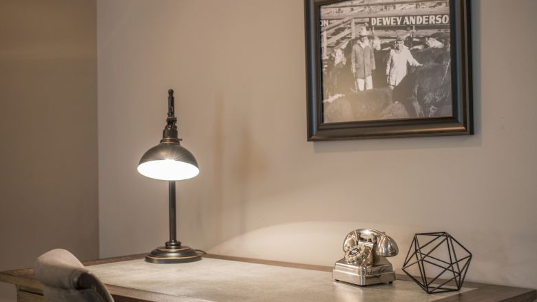 A desk with a vintage phone, geometric decor, and a lamp. A framed photo labeled 