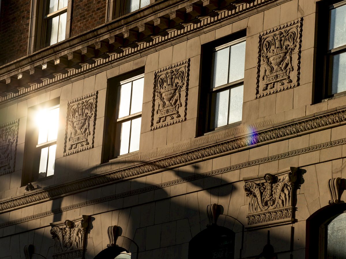 A building facade with ornate decorations, windows reflecting sunlight, and intricate architectural details casting shadows.