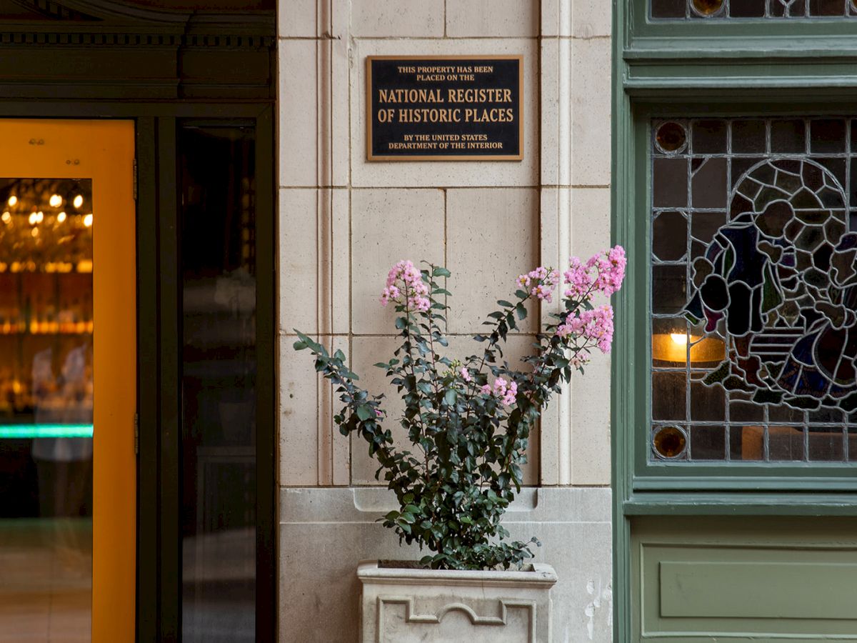 A plant in front of a building with a plaque indicating it's on the National Register of Historic Places, beside a stained glass window.