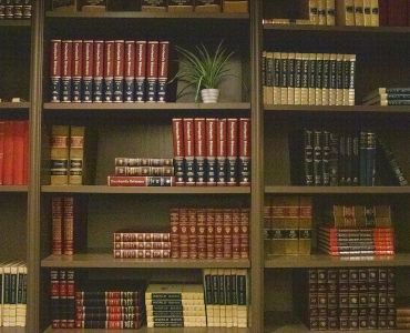 A bookshelf filled with various books, including encyclopedias, and a small potted plant in the center.