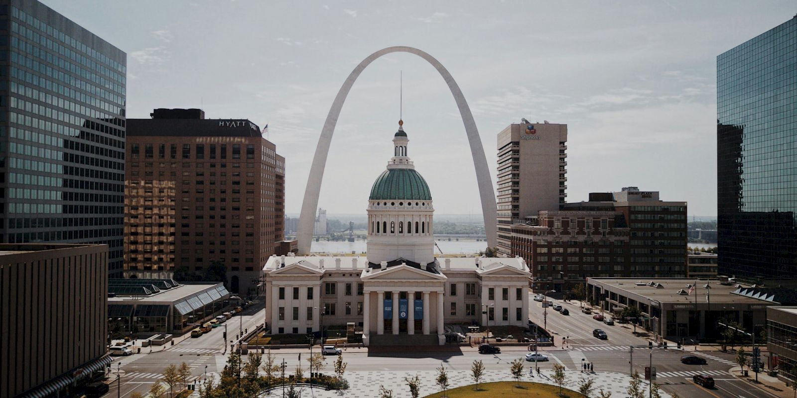 The image shows the Old Courthouse and the Gateway Arch in St. Louis, surrounded by city buildings under a clear sky.