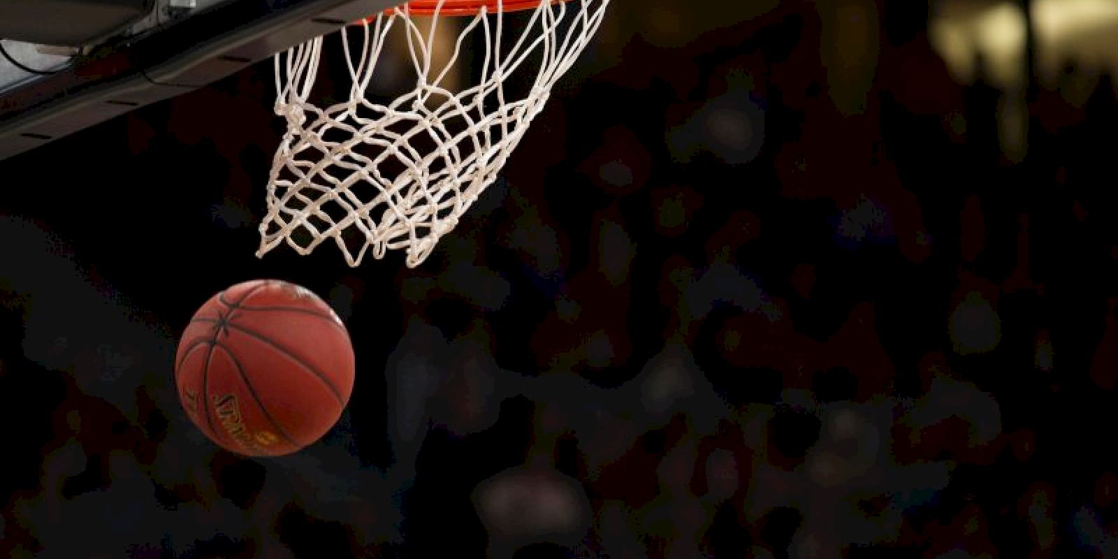 A basketball is about to go through a hoop in an action shot, with a dark background highlighting the scene.
