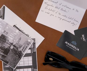 Black and white photos, a handwritten note, Magnolia Hotel cards, and sunglasses are arranged on a surface.