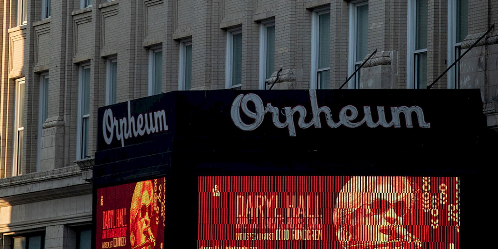 The image shows the Orpheum theater with signs promoting a performance by Daryl Hall, under a glass walkway in front of a building.