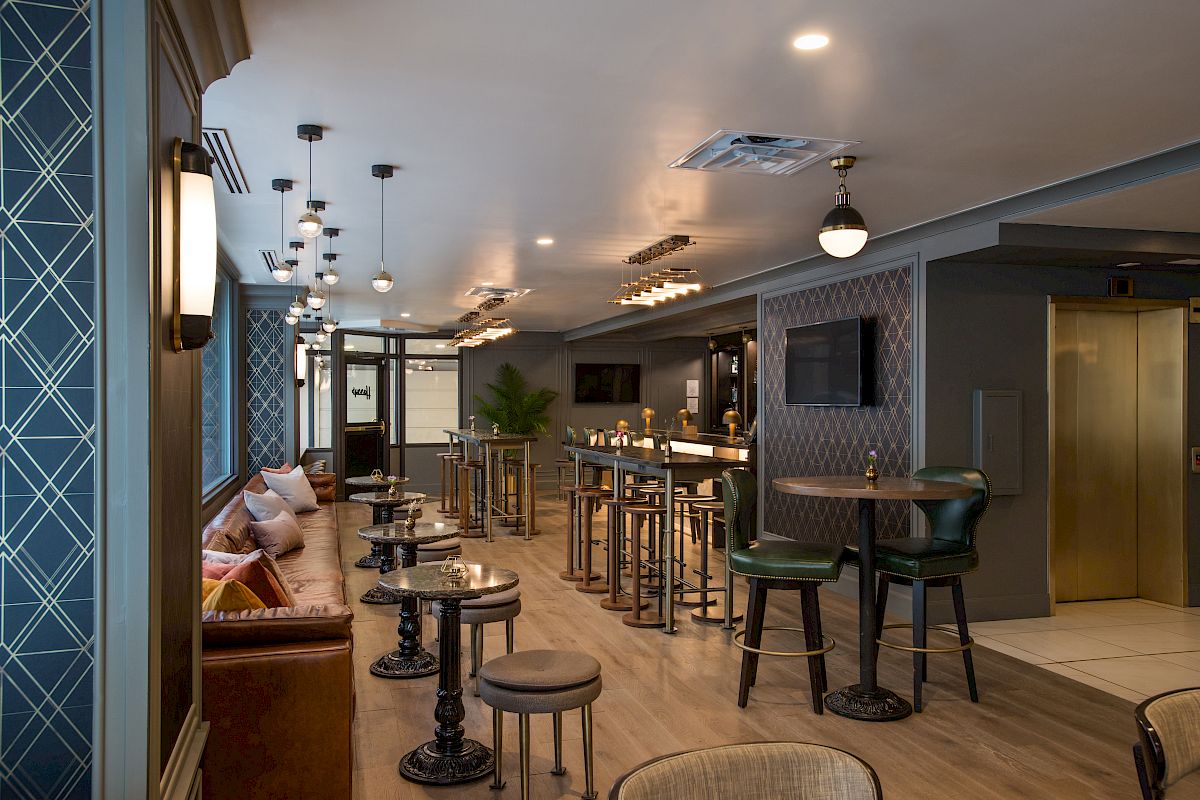 A stylish lounge with patterned walls, cushioned seating, high tables, and modern lighting creates a cozy and elegant atmosphere.